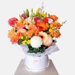 Orange toned flowers in a round white  presentation box